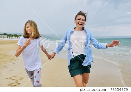 Happy mom and daughter running on the sea beach holding hands 78354879