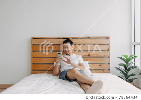 Happy Asian man feels relax with smartphone on his bed. 78364434