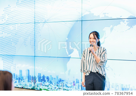 A woman explaining with a microphone in front of a large screen A woman explaining with a microphone in front of a large screen 78367954
