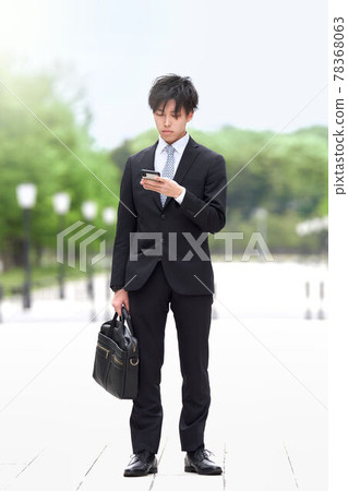 一個年輕的商人站著看智能手機 78368063