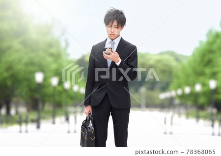 A young businessman who stops and looks at his smartphone 78368065