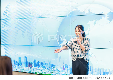 A woman explaining with a microphone in front of a large screen A woman explaining with a microphone in front of a large screen 78368395