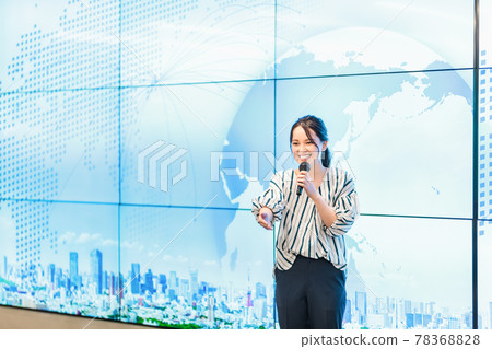 A woman explaining with a microphone in front of a large screen A woman explaining with a microphone in front of a large screen 78368828