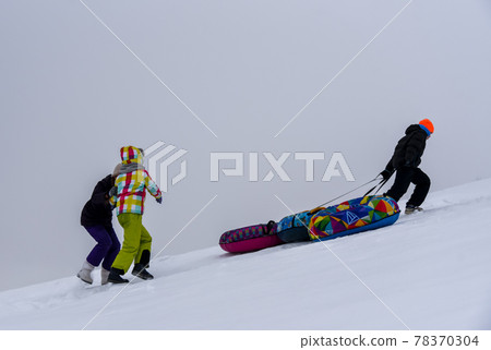 Teen helps friends pull tubing down a snow slide 78370304