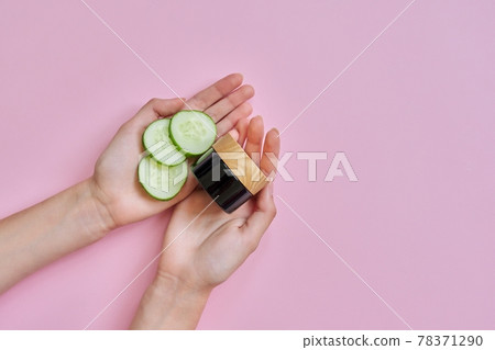 Woman's hands with glass bottle, cucumber slices on pink background 78371290