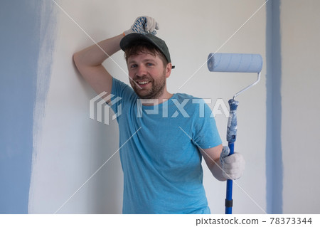Young painter in blue t-shirt, cap and gloves painting a wall with paint roller. 78373344