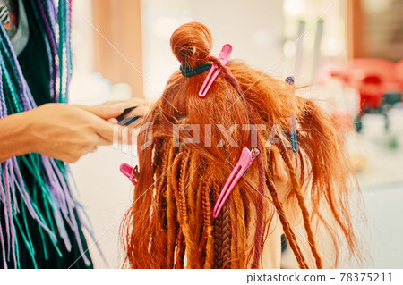 Hairdresser weaves braids with red kanekalon beautiful red-head girl. 78375211