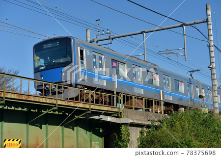 Seibu Line 20000 series train with blue line crosses Iruma River iron bridge in autumn blue sky, aluminum body Seibu Line 20000 series train with blue line crosses Iruma River iron bridge in autumn blue sky, aluminum body 78375698