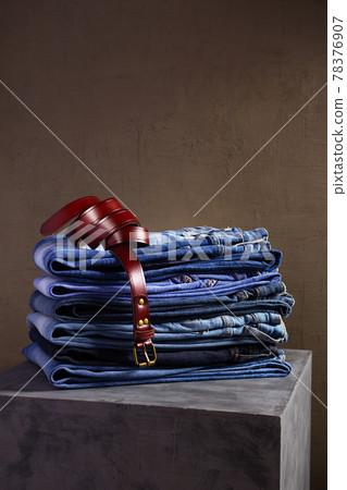 Denim jeans and leather belt at old grey cube near grey wall background.  Stack of jeans 78376907