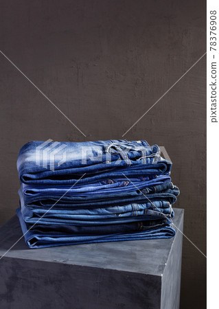 Denim jeans at old grey cube near grey wall background texture.  Stack of jeans 78376908