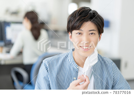 一個休閒風格的年輕商人,他在辦公室裡摘下面具微笑 一個休閒風格的年輕商人,他在辦公室裡摘下面具微笑 78377016