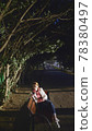woman in white leather jacket use smartphone while sitting on a park bench 78380497