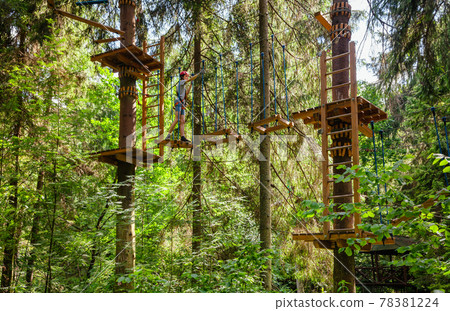 Teen boy on a ropes course in a treetop adventure park passing hanging rope obstacle Teen boy on a ropes course in a treetop adventure park passing hanging rope obstacle 78381224