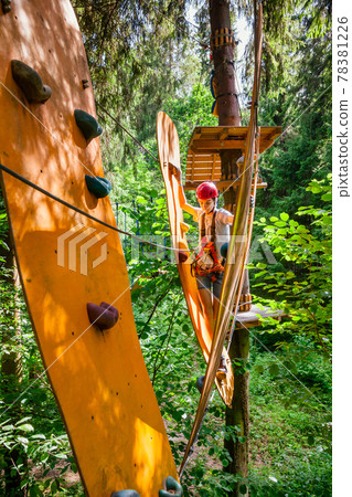 Teen boy on a ropes course in a treetop adventure park passing hanging rope bridge obstacle 78381226