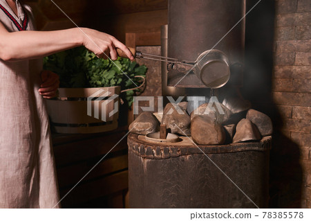 woman in a bath pours water on hot stones on the stove woman in a bath pours water on hot stones on the stove 78385578