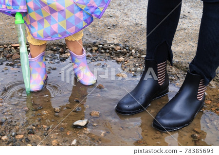 Children's and mom's boots entering a puddle during the rainy season in June 78385693
