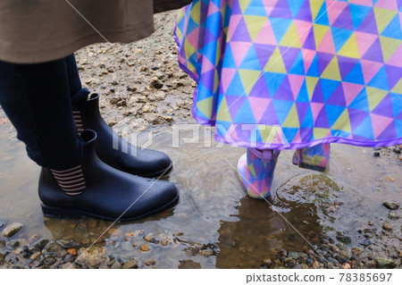 Children's and mom's boots entering a puddle during the rainy season in June Children's and mom's boots entering a puddle during the rainy season in June 78385697