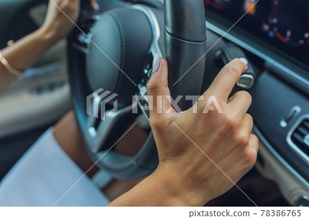 Woman's hand switches the lobes of the gear selector on the steering wheel. Hand is switching car gear lever, close up shot of a manual gear changing paddle on a car's steering wheel. Woman's hand switches the lobes of the gear selector on the steering wheel. Hand is switching car gear lever, close up shot of a manual gear changing paddle on a car's steering wheel. 78386765