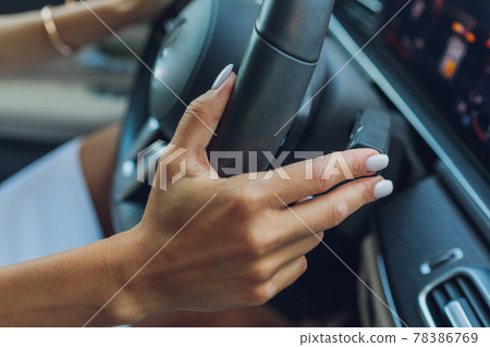 Woman's hand switches the lobes of the gear selector on the steering wheel. Hand is switching car gear lever, close up shot of a manual gear changing paddle on a car's steering wheel. Woman's hand switches the lobes of the gear selector on the steering wheel. Hand is switching car gear lever, close up shot of a manual gear changing paddle on a car's steering wheel. 78386769