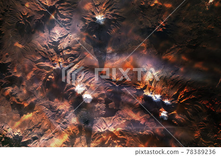 Collage with red lava reflections of several snow- and ice-capped volcanoes over a mountainous region of Bolivia and Chile. 78389236