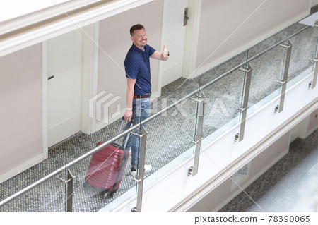 Young smiling man stands in hotel corridor and shows thumbs up gesture 78390065