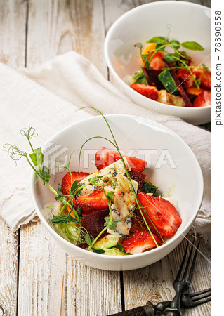 Vertical shot delicious summer salad. Salad with fresh strawberries, baked beets, yellow tomatoes, dor blue cheese and herbs in a white bowl on a light rustic background. Summerfood. Close-up 78390558