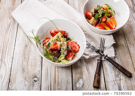 Delicious summer salad. Salad with fresh strawberries, baked beets, yellow tomatoes, dor blue cheese and herbs in a white bowl on a light rustic background. Top view. Copy space. Summerfood 78390562