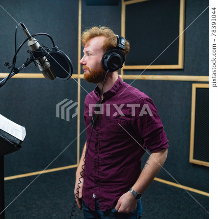 Bearded young man stay near microphone, recording voice in professional studio Bearded young man stay near microphone, recording voice in professional studio 78391044