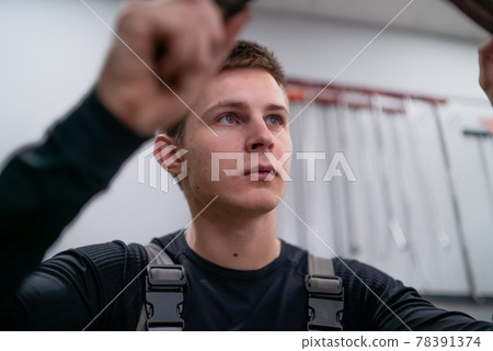 Concentrated blue eyes sight of young car repair specialist leveling harmed part 78391374