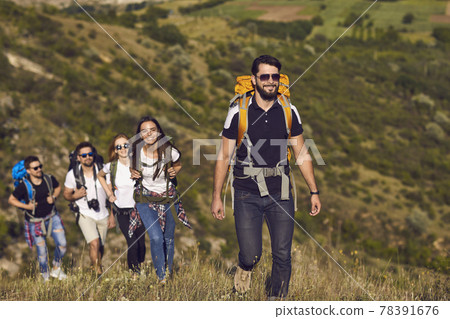 Group of smiling young travelers hikers tourists with backpacks hiking with in row 78391676