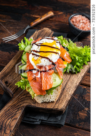 Smoked salmon Sandwich with Benedict egg and avocado on bread. Dark wooden background. Top view Smoked salmon Sandwich with Benedict egg and avocado on bread. Dark wooden background. Top view 78392816