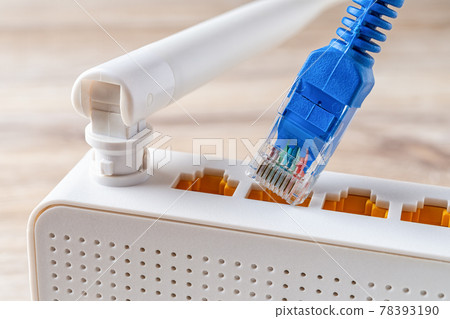 Close-up of blue network cable plug almost inserting into the socket of the white Wi-Fi router. 78393190