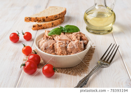 Canned tuna meat in a bowl, fork, bread and fresh red cherry tomatoes on a white wooden table. Canned tuna meat in a bowl, fork, bread and fresh red cherry tomatoes on a white wooden table. 78393194