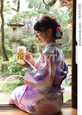 A young woman in a yukata drinking beer on the porch 78395385