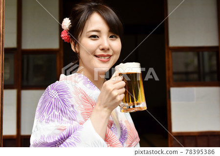 一個穿著浴衣在門廊上喝啤酒的年輕女人 一個穿著浴衣在門廊上喝啤酒的年輕女人 78395386