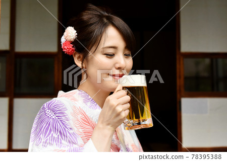 一個穿著浴衣在門廊上喝啤酒的年輕女人 一個穿著浴衣在門廊上喝啤酒的年輕女人 78395388