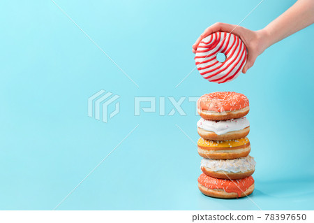 Stack of donuts, donut in hand on blue, copy space 78397650