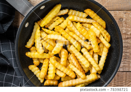Fried Crinkle oven French fries potatoes sticks in a pan. Wooden background. Top view Fried Crinkle oven French fries potatoes sticks in a pan. Wooden background. Top view 78398721