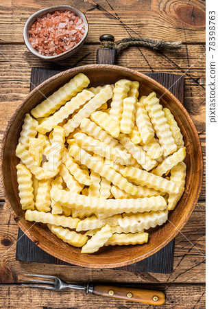 Frozen Crinkle oven French fries potatoes sticks in a wooden plate. Wooden background. Top view Frozen Crinkle oven French fries potatoes sticks in a wooden plate. Wooden background. Top view 78398763