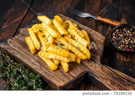Baked Crinkle French fries potatoes sticks or chips on a wooden board. Dark wooden background. Top view Baked Crinkle French fries potatoes sticks or chips on a wooden board. Dark wooden background. Top view 78399150