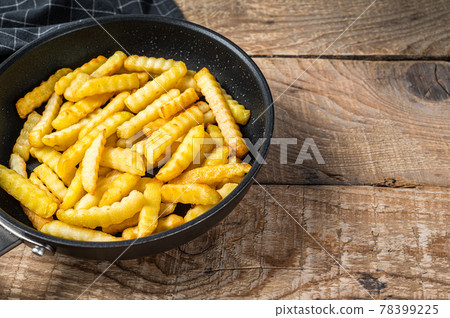 Fried Crinkle oven French fries potatoes sticks in a pan. Wooden background. Top view. Copy space Fried Crinkle oven French fries potatoes sticks in a pan. Wooden background. Top view. Copy space 78399225