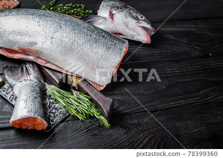 Raw cut salmon fish on a wooden cutting board with chef cleaver. Black Wooden background. Top view. Copy space 78399360