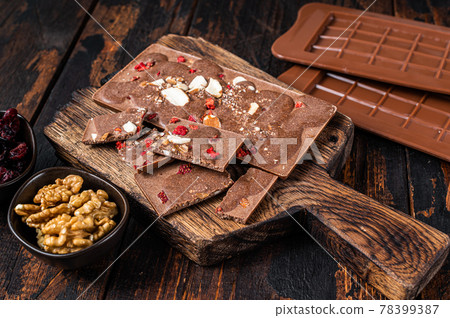 Homemade Craft milk chocolate bar with hazelnuts, peanuts, cranberries and freeze dried raspberries. Dark wooden background. Top view Homemade Craft milk chocolate bar with hazelnuts, peanuts, cranberries and freeze dried raspberries. Dark wooden background. Top view 78399387