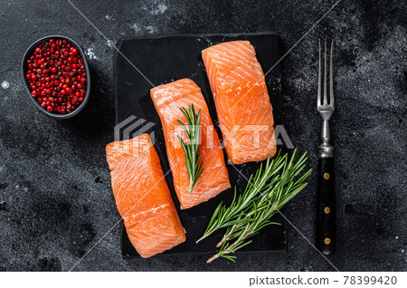 Raw salmon fillet steaks on marble board with herbs. Black background. Top view Raw salmon fillet steaks on marble board with herbs. Black background. Top view 78399420