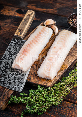 Raw cod loin fillet steak on wooden board with butcher cleaver. Dark wooden background. Top view Raw cod loin fillet steak on wooden board with butcher cleaver. Dark wooden background. Top view 78399456