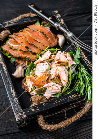 Toasts with hot and cold smoked salmon, arugula in a wooden tray with herbs. Black wooden background. Top view Toasts with hot and cold smoked salmon, arugula in a wooden tray with herbs. Black wooden background. Top view 78399618