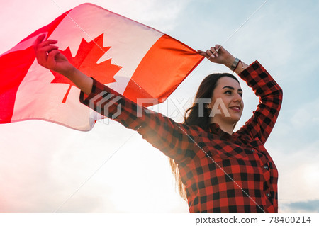 Young millennial brunette woman holding The National Flag of Canada. Canadian Flag or the Maple Leaf. Tourist traveler or patriotism. Immigrant in a free country. Independence day 1th july Young millennial brunette woman holding The National Flag of Canada. Canadian Flag or the Maple Leaf. Tourist traveler or patriotism. Immigrant in a free country. Independence day 1th july 78400214