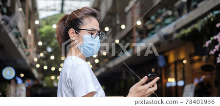 Woman wearing medical face mask and using smartphone during walking in night market, prevent coronavirus or Corona Virus Disease (Covid-19). Health, life concept Woman wearing medical face mask and using smartphone during walking in night market, prevent coronavirus or Corona Virus Disease (Covid-19). Health, life concept 78401936