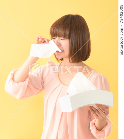A young woman holding a tissue box and blowing her nose with a painful face 78402009