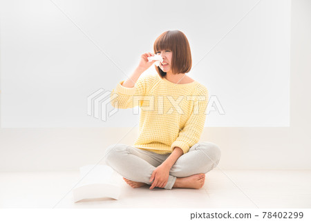 A young woman with a painful face sitting on the floor and holding her nose with tissue A young woman with a painful face sitting on the floor and holding her nose with tissue 78402299